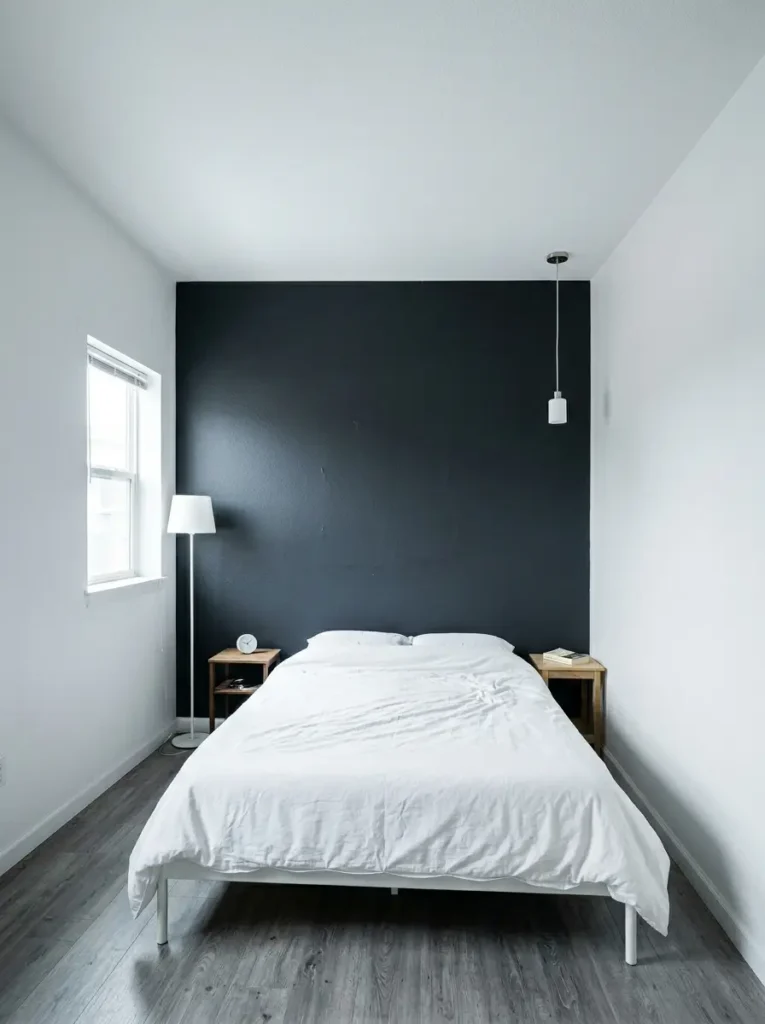 Small bedroom featuring a solid black accent wall behind a white bed with minimal lighting
