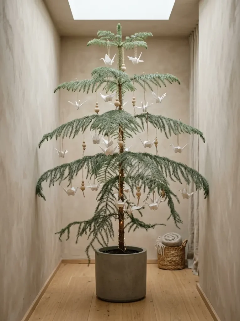 Sparse evergreen tree in a concrete pot decorated solely with folded white paper cranes and wooden beads