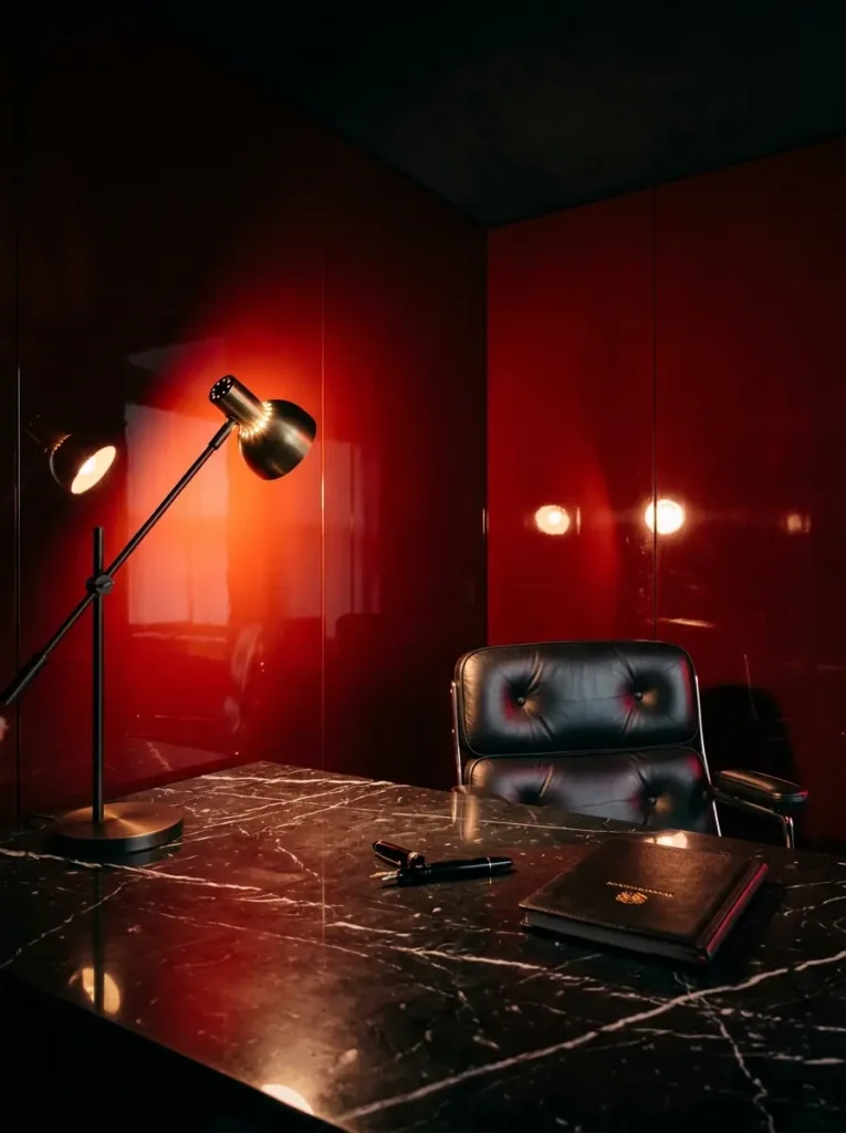 Desk lamp bouncing light off high gloss red walls in a dark apartment study.
