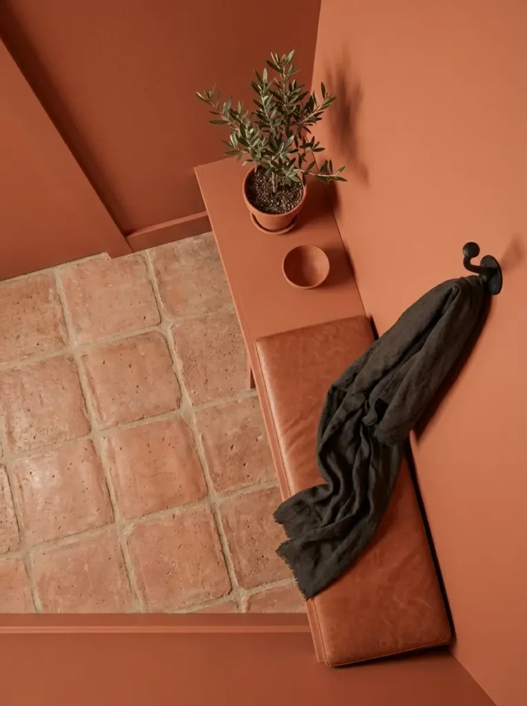 Terracotta painted walls match square clay floor tiles around a slim console table and leather bench.