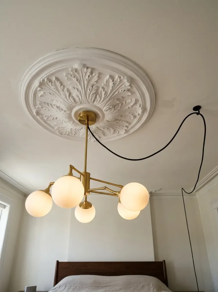 White floral ceiling medallion framing a brass plug in chandelier