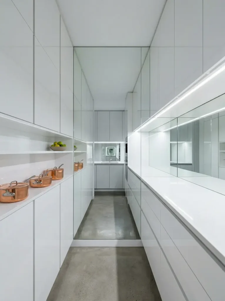 Reflective glass backsplash in a narrow white galley kitchen