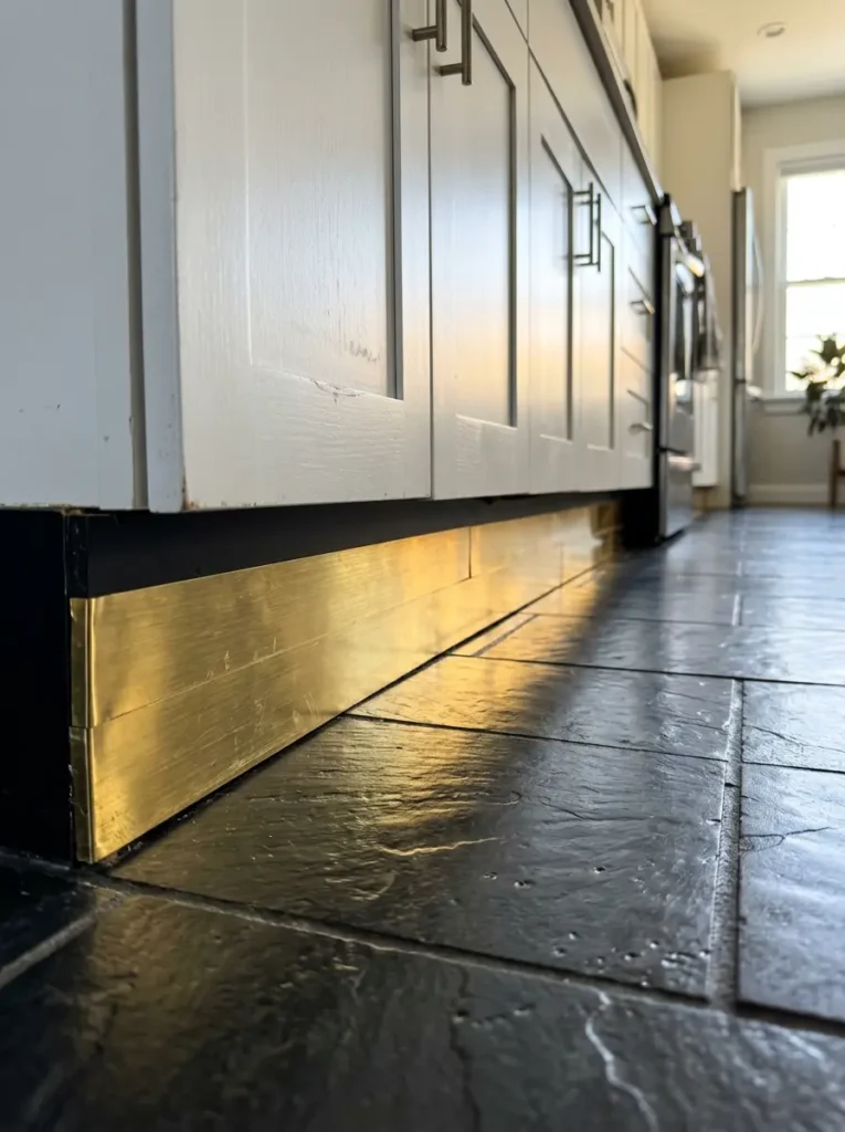 Metallic brass tape applied to the base toe kick of white kitchen cabinets