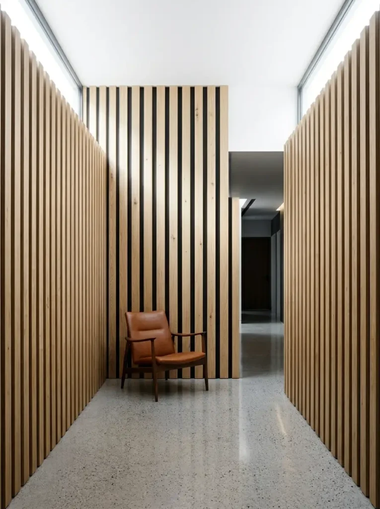 Vertical Wood Slat Walls Hallway walls covered in vertical light oak wood slats separated by dark gaps behind a leather chair.