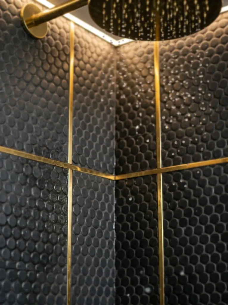 Golden metal strips inserted between dark circular mosaic shower tiles