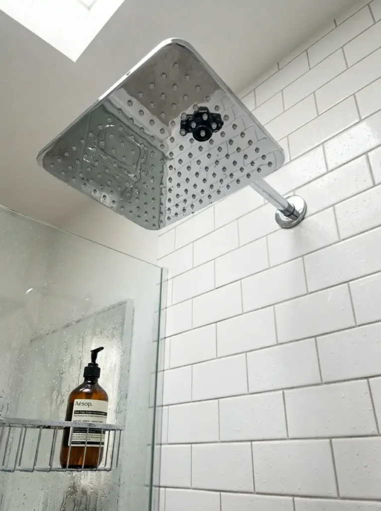 Large square chrome rainfall showerhead installed in a white subway tile shower