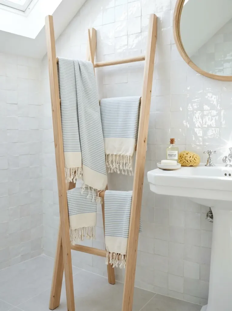 Wooden towel ladder leaning against white bathroom tile.
