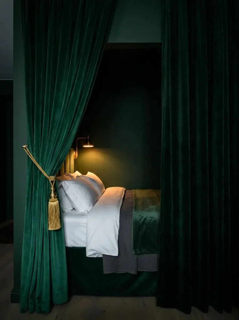 Heavy emerald green velvet curtains frame a cozy recessed bed