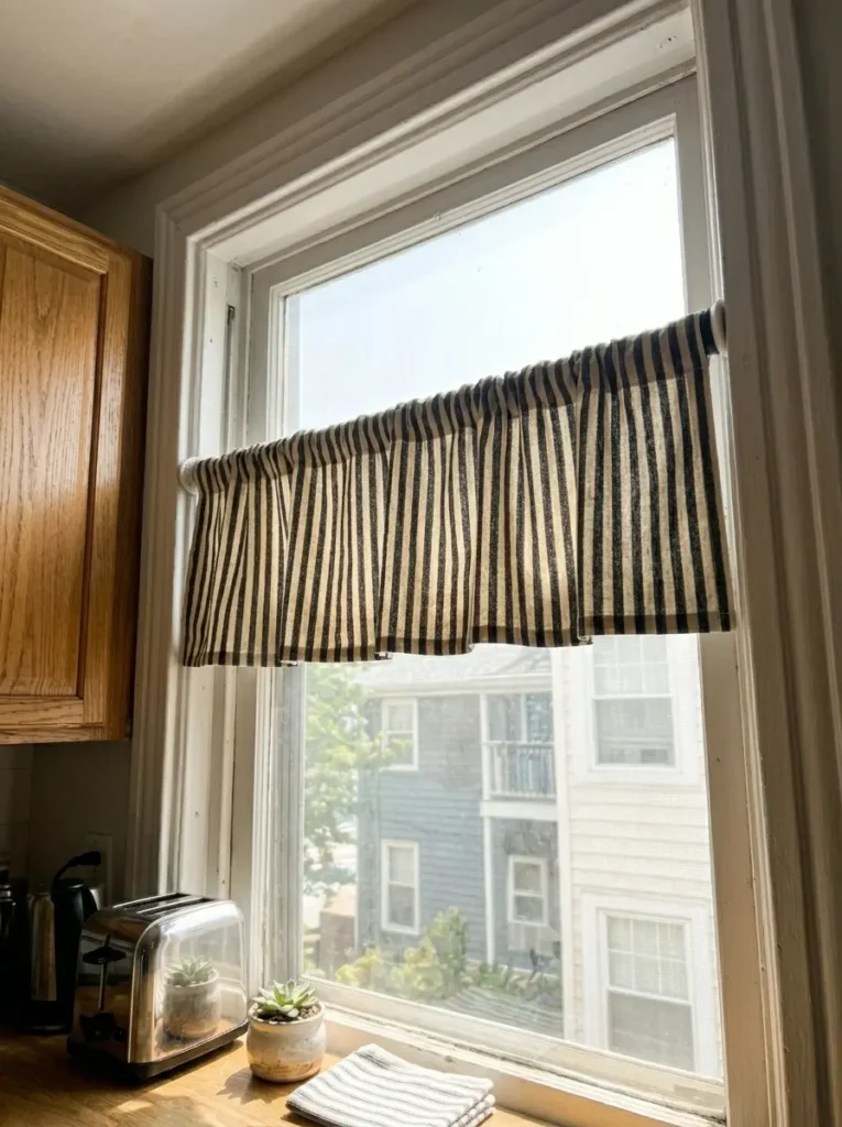 Black and white striped fabric draped over a tension rod for a cheap window treatment