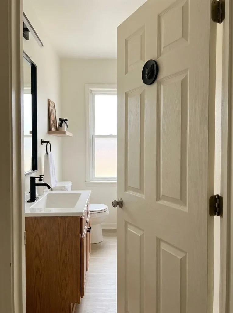 Three-quarter hallway view of a black cat medallion on an open bathroom door with the vanity visible beyond.