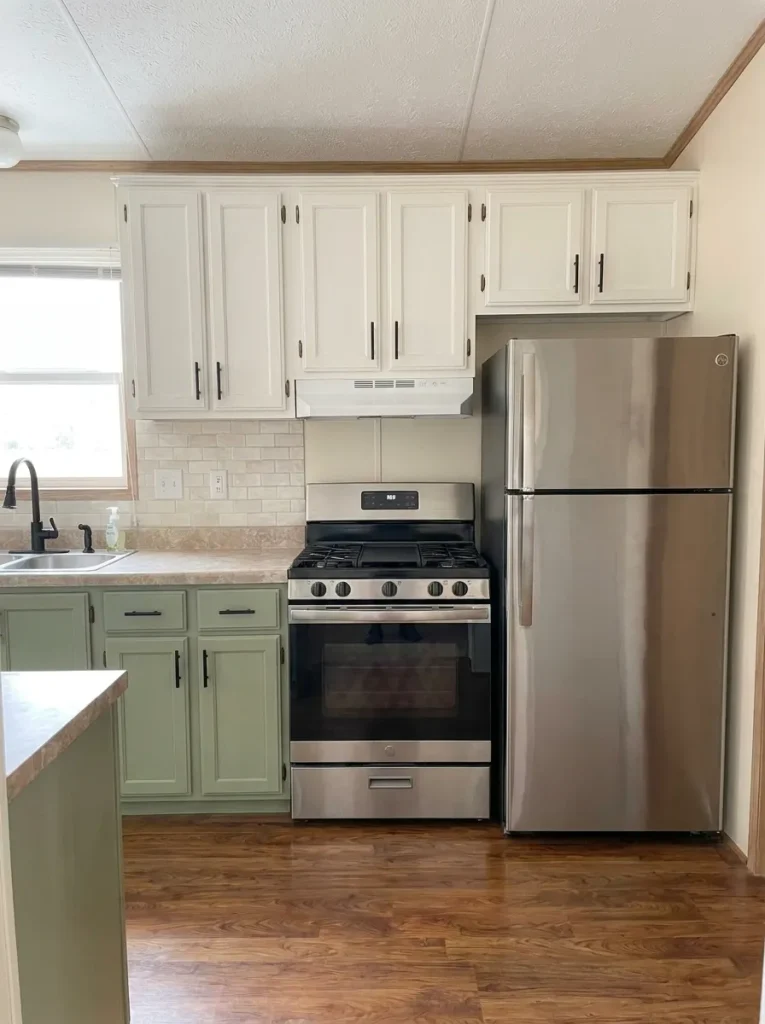 Existing stainless and black appliances integrated into a mobile-home kitchen with sage, warm white and natural wood finishes.