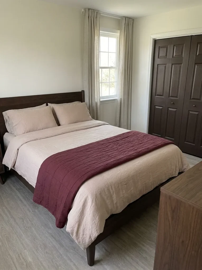 Burgundy quilt on blush-beige bedding with an espresso bed frame and dark closet doors beyond.