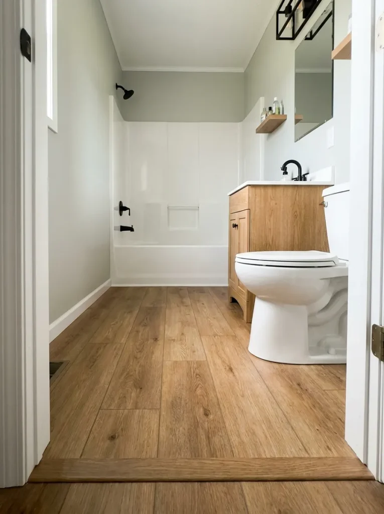 Continuous visible flooring leading through a narrow mobile home bathroom.