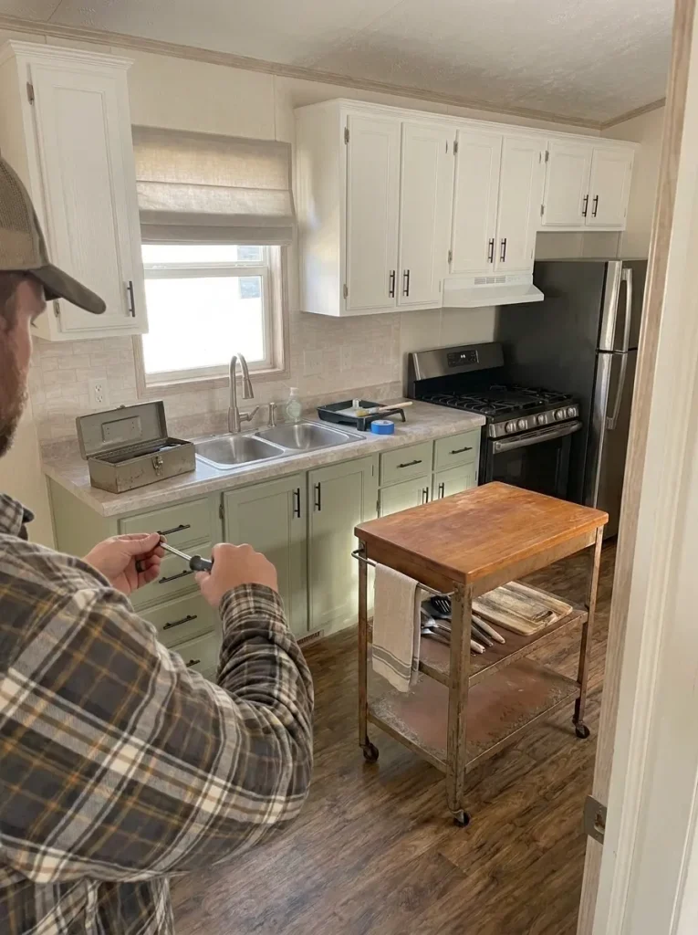 Homeowner completing a cosmetic cabinet update while the mobile-home kitchen's plumbing, electrical and structural systems remain untouched.