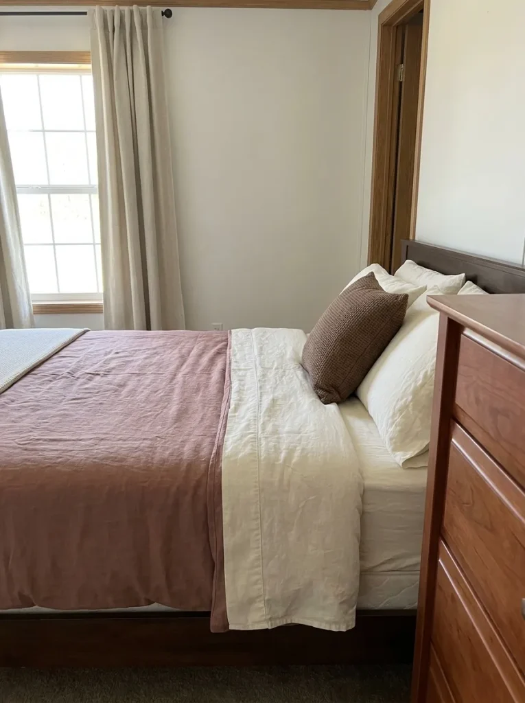 Dusty-rose bedding with warm-white sheets and a cocoa cushion beside a cherry-toned dresser.
