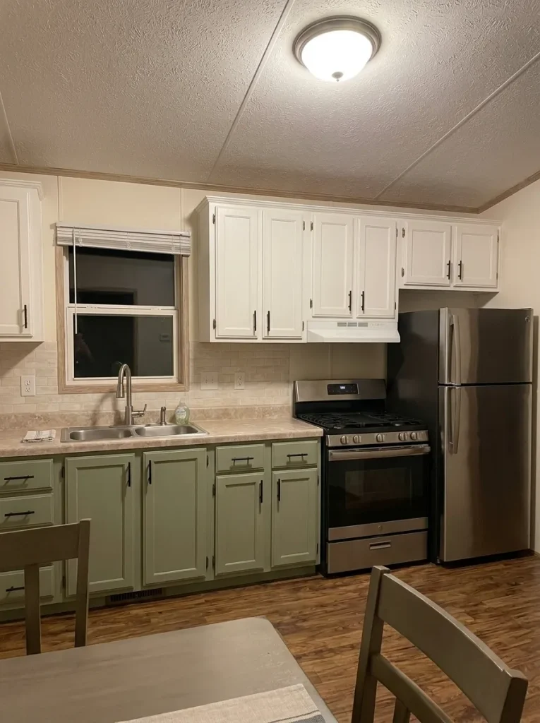 Evening mobile-home kitchen where the ceiling light brightens the room but leaves part of the prep counter in shadow.