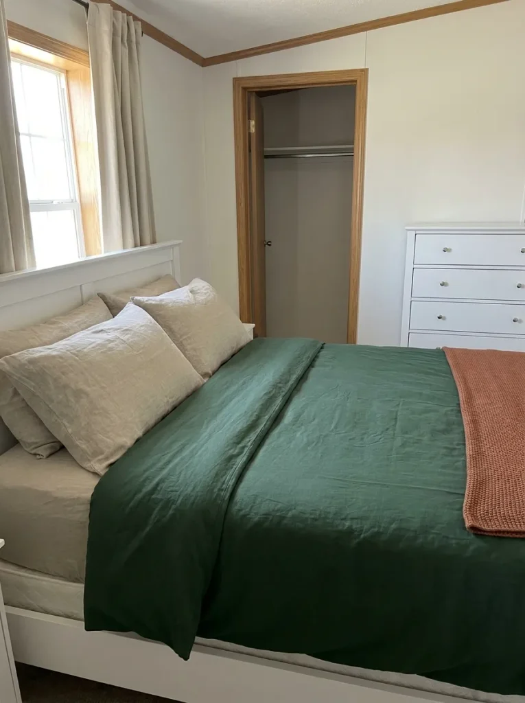 Forest-green duvet with flax pillows and a terracotta throw beside pale walls and bedroom closet doors.