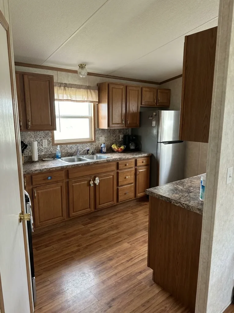 Sound mobile home kitchen with usable cabinets and flooring but competing surfaces and mismatched hardware ready for selective updating.