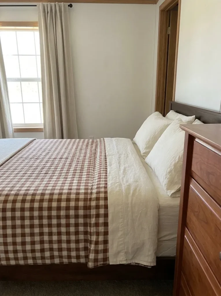 Chestnut-and-oatmeal gingham duvet with cream pillows and solid curtains in a small bedroom.