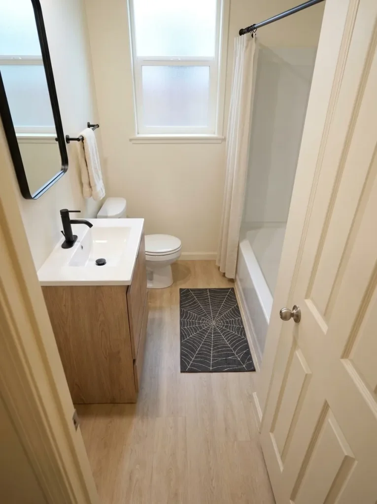 High-angle view of a rectangular spiderweb mat with clear floor around the vanity, toilet, and tub.