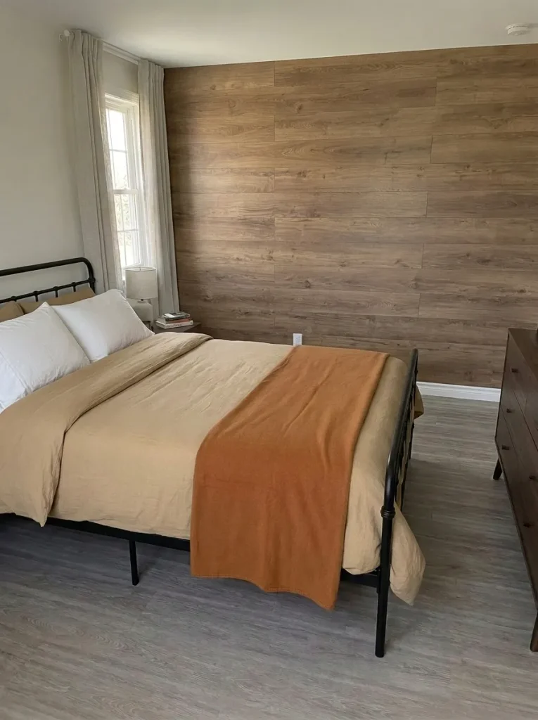 Elevated diagonal view of wheat bedding, a caramel throw, and white pillows against wood-look wall panels.