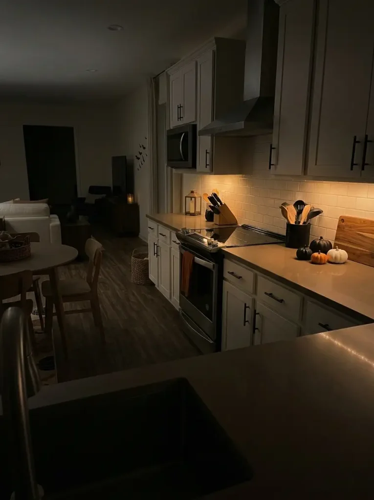 Cozy Halloween small mobile-home kitchen uses warm textiles, wood, and amber lighting while keeping the main countertops clear for cooking.