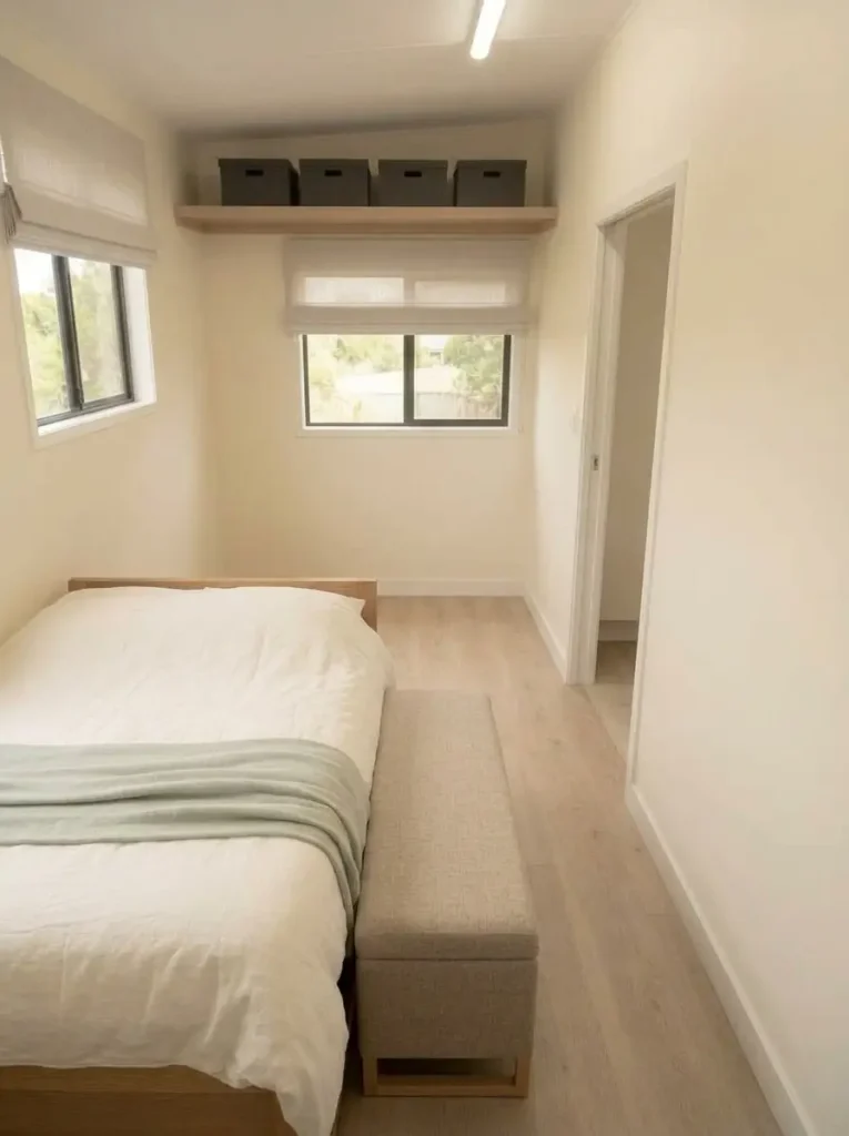 Narrow storage bench at the foot of a bed with a clear walkway toward the bedroom door.