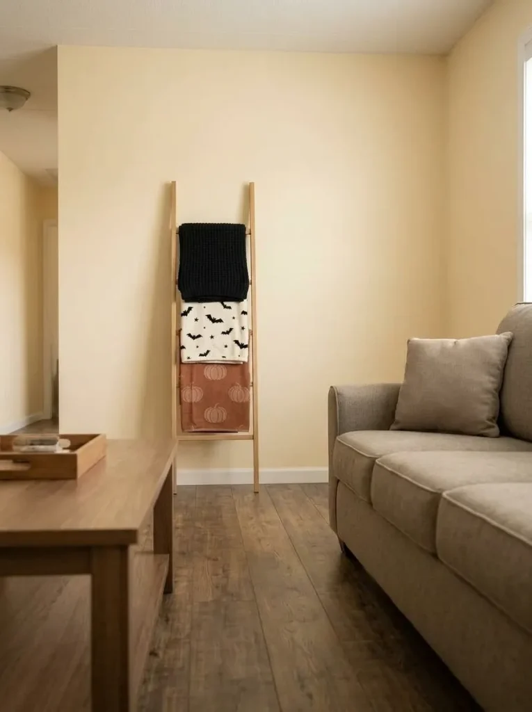Halloween-patterned blankets displayed vertically on a ladder beside an uncluttered neutral sofa in a mobile home.