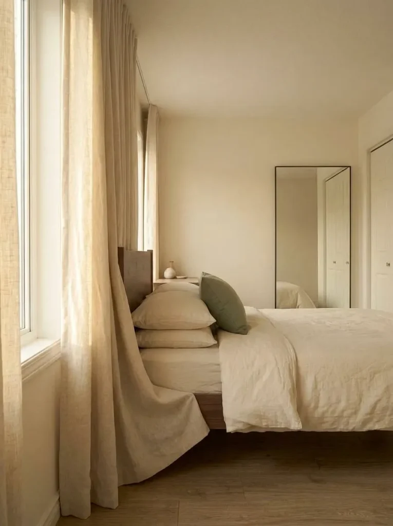 Window-side view across a mobile home bedroom showing curtains, bed, and headboard composed as one balanced sleeping zone.