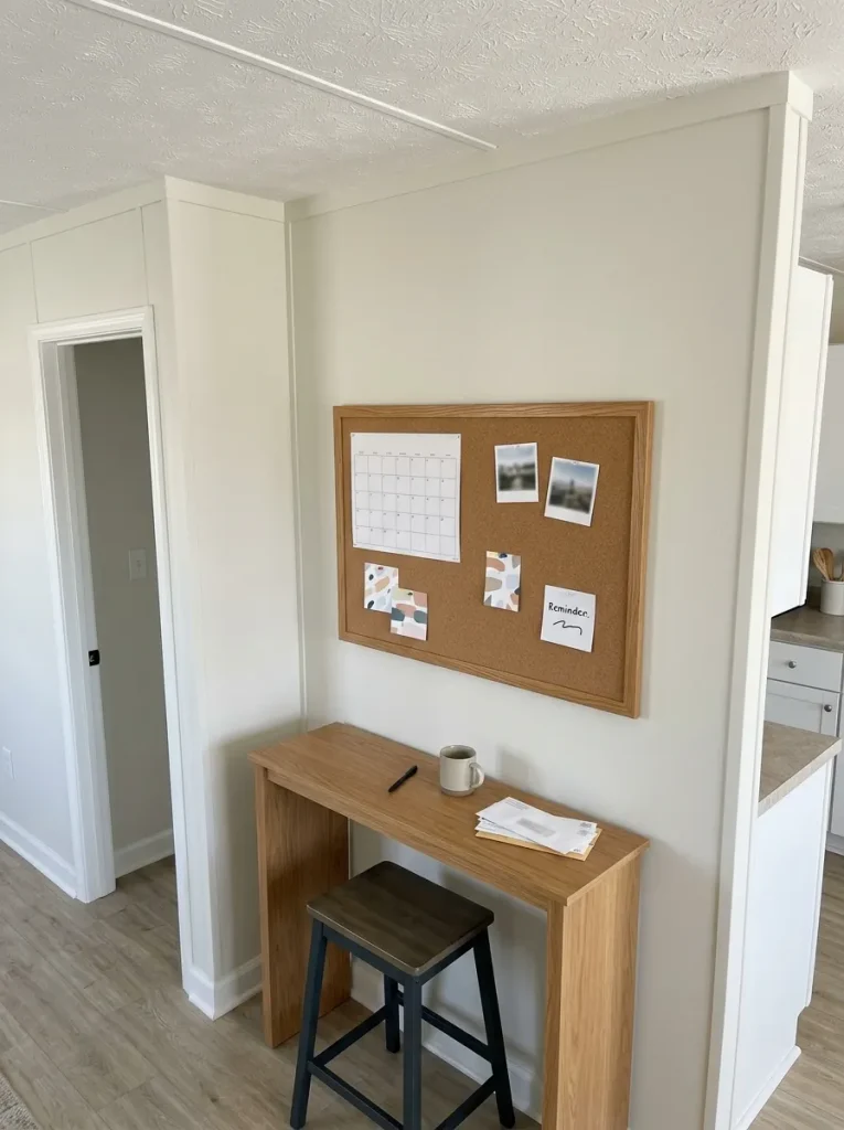 Small mobile home command area with a framed cork board beside a compact desk and neatly grouped household notes.