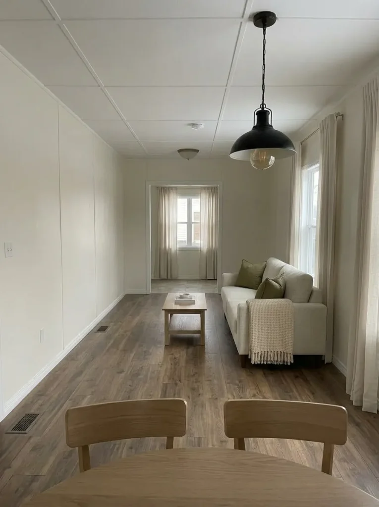 Mobile home open interior with one high-visibility wall painted a calm warm neutral across connected living and dining areas.
