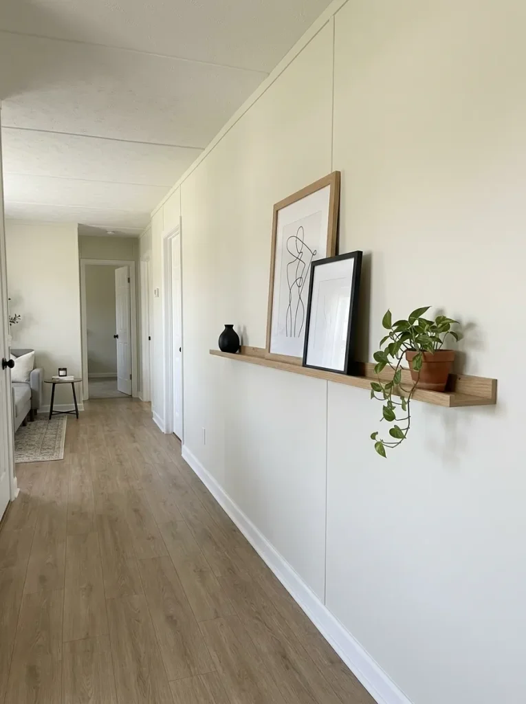 Long mobile home wall with a slim oak picture ledge holding a few overlapping frames while much of the wall remains open.