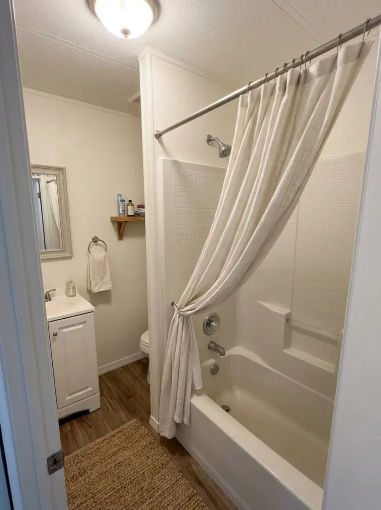 Light shower curtain reduces visual bulk around an existing tub in a small mobile-home bathroom.