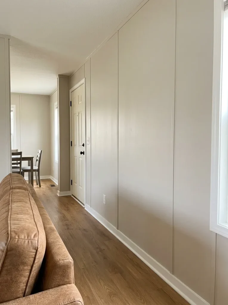 Single-wide mobile home living wall with original vertical battens painted the same warm greige as the surrounding wall panels.