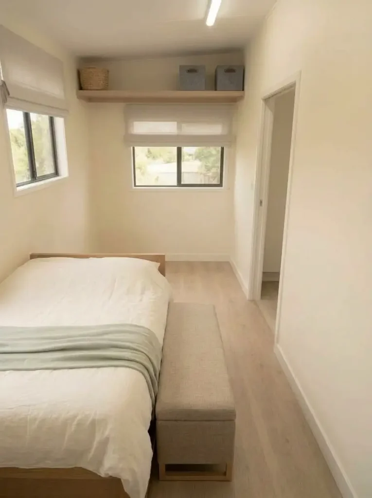 Open bedroom shelving with matching baskets and empty space creating a calmer storage wall in a mobile home bedroom.