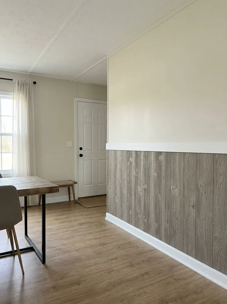 Mobile home dining area with weathered wood wainscoting below a light cream upper wall and restrained flooring.