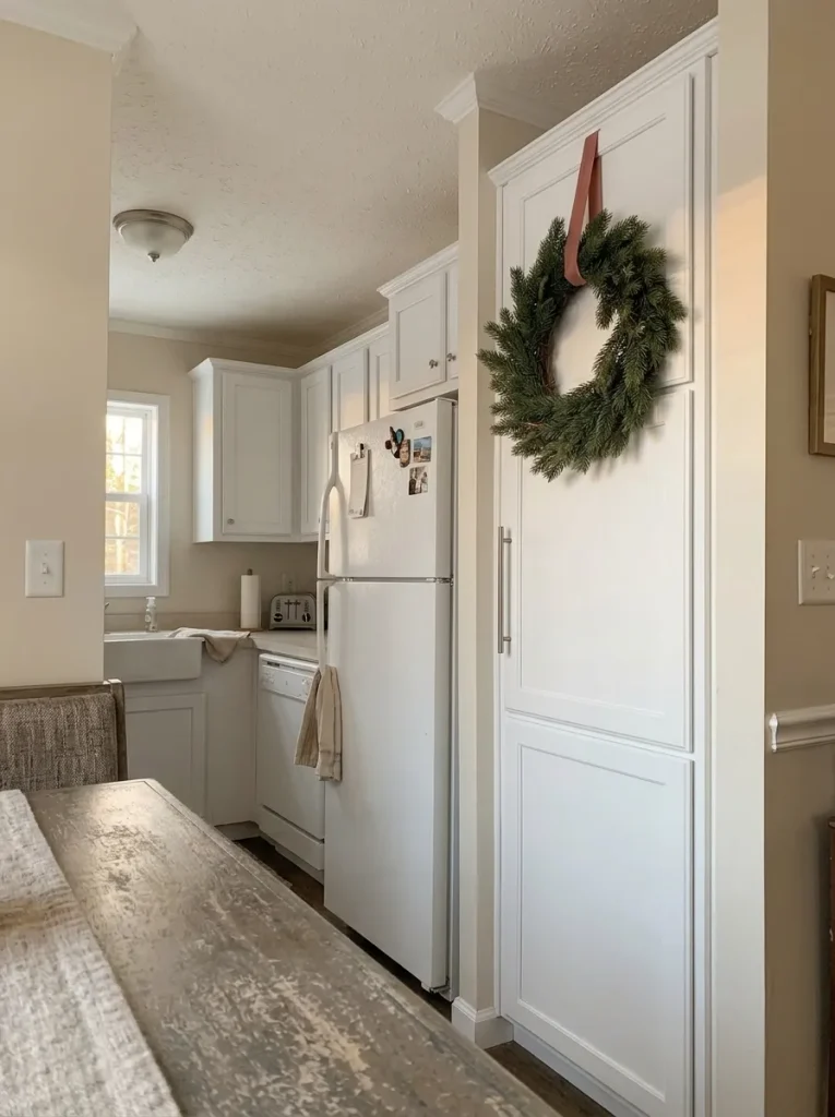 Tall mobile home kitchen pantry cabinet decorated with one larger evergreen Christmas wreath beside a breakfast nook.