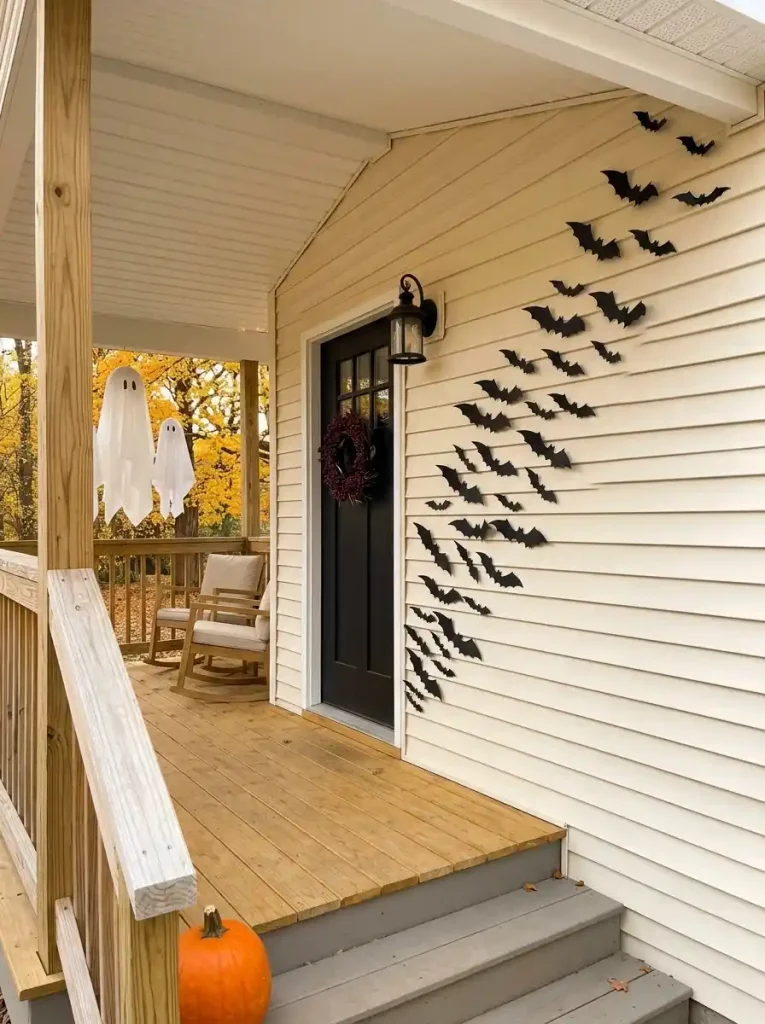 Black bat silhouettes rise diagonally from the front door toward an upper porch corner on a cream mobile home exterior.