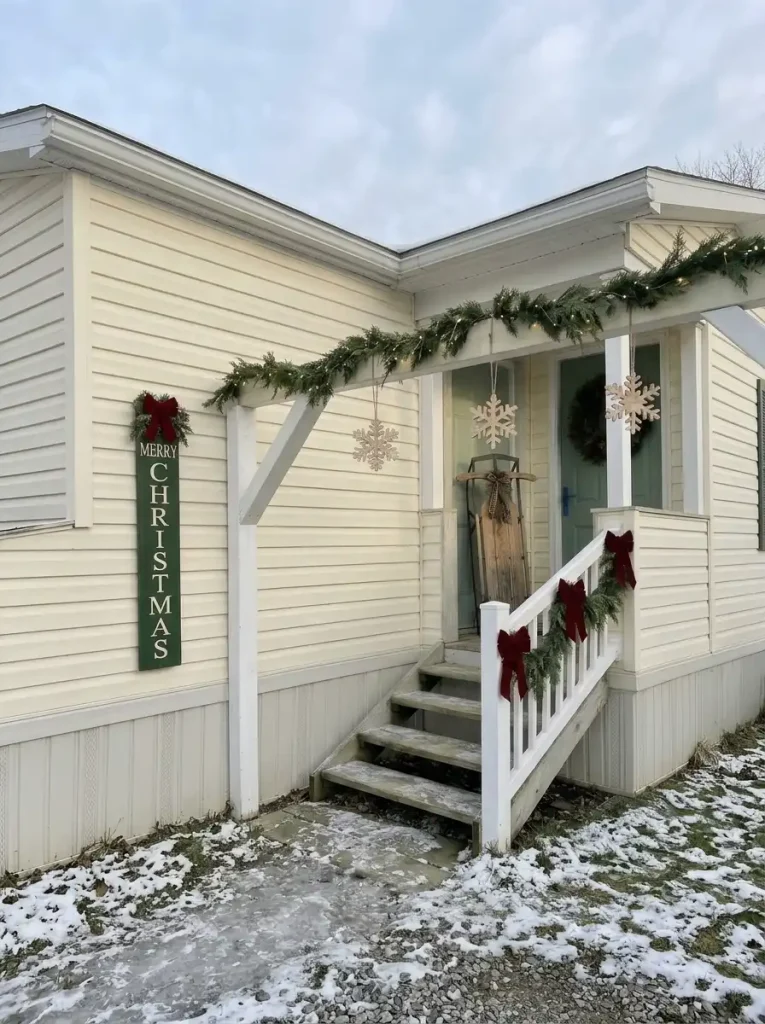 Forest-green Merry Christmas wooden sign with evergreen accents beside a compact mobile-home entrance.