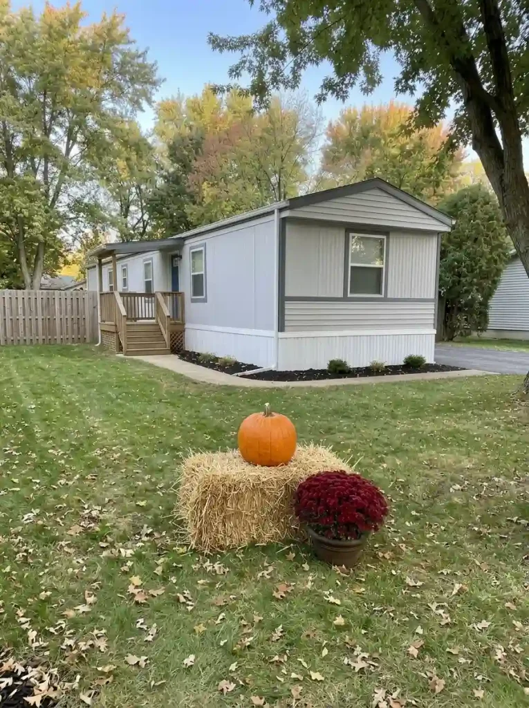 Broad pumpkin on one straw bale beside a burgundy mum pot in a mobile home front yard.
