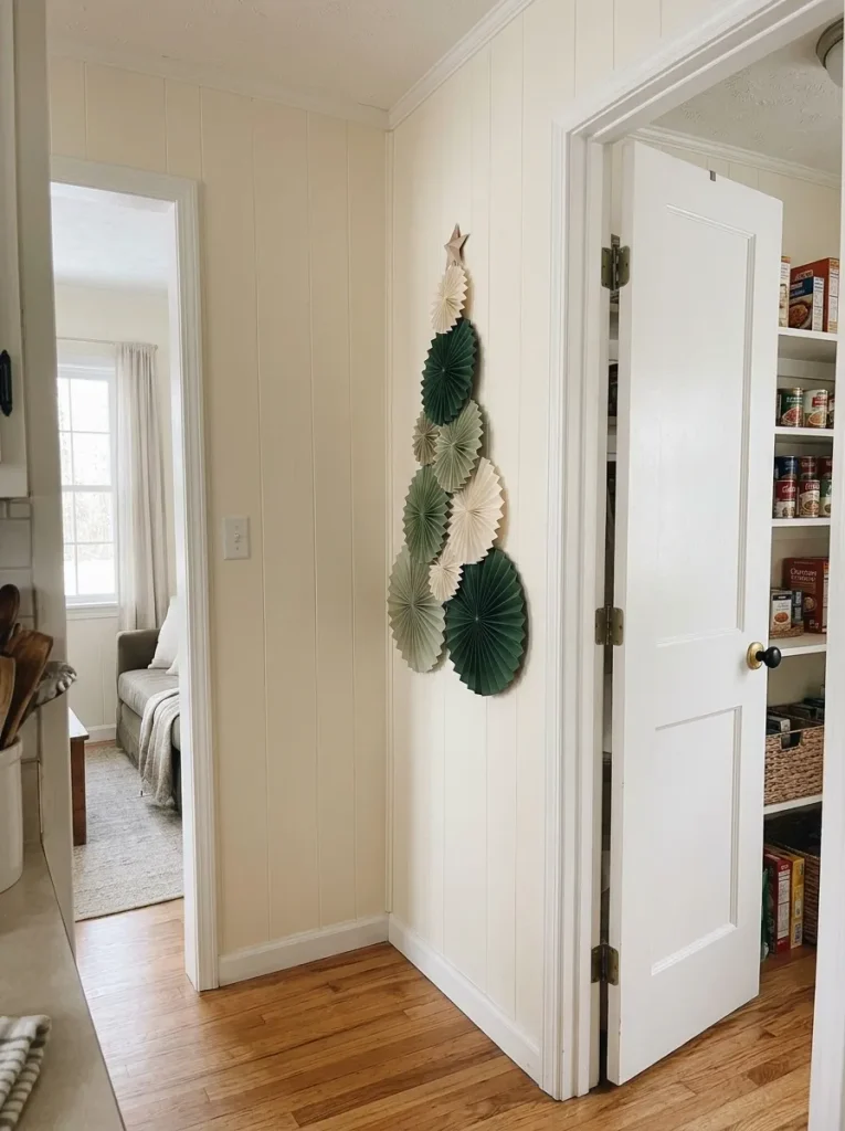 Folded green paper fans arranged into a flat Christmas tree on a narrow wall beside a mobile-home pantry.