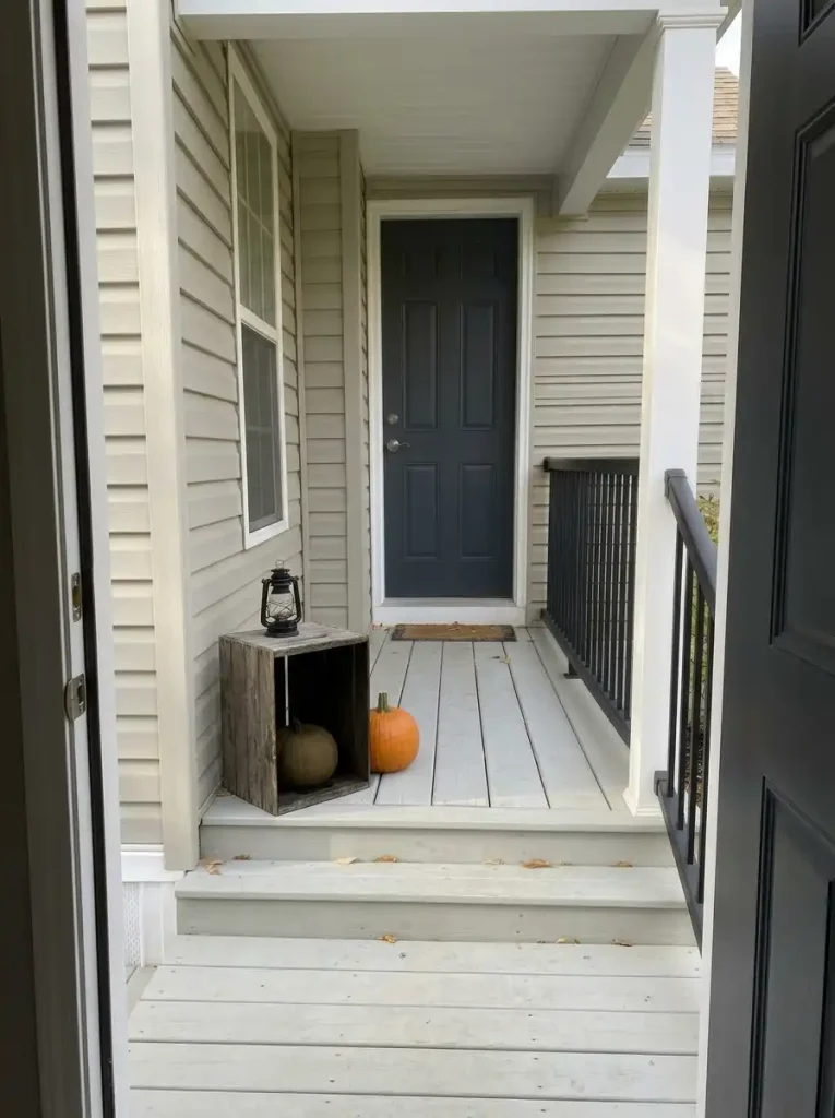 Cream pumpkin displayed inside a single wooden crate cubby with a lantern and orange pumpkin on a mobile-home porch.