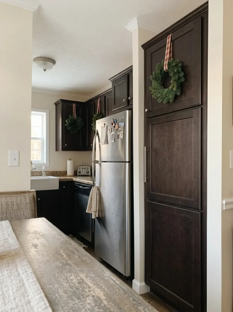 Espresso kitchen cabinets in a mobile home decorated with mini evergreen wreaths and red plaid ribbons.