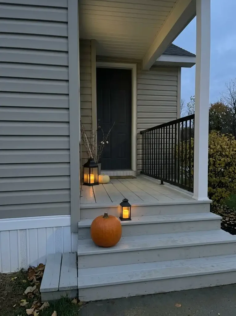 Simplified late-fall mobile-home porch retains its main pumpkin clusters and lanterns after extra flowers and foliage are removed.
