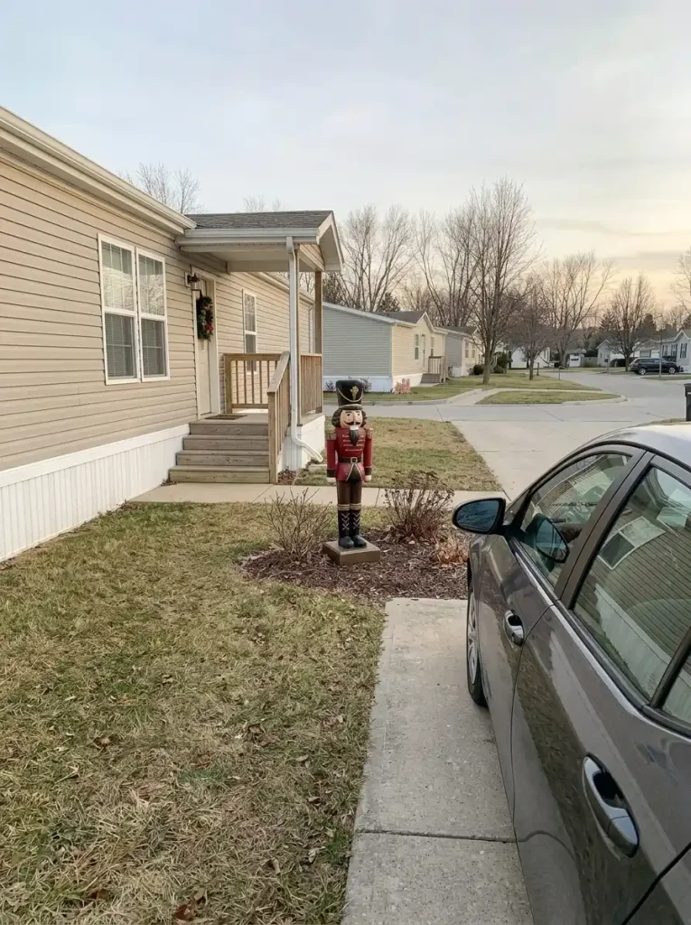 Single outdoor nutcracker standing in a landscape pocket beside a parked car and a manufactured-home driveway, with clear passenger access.
