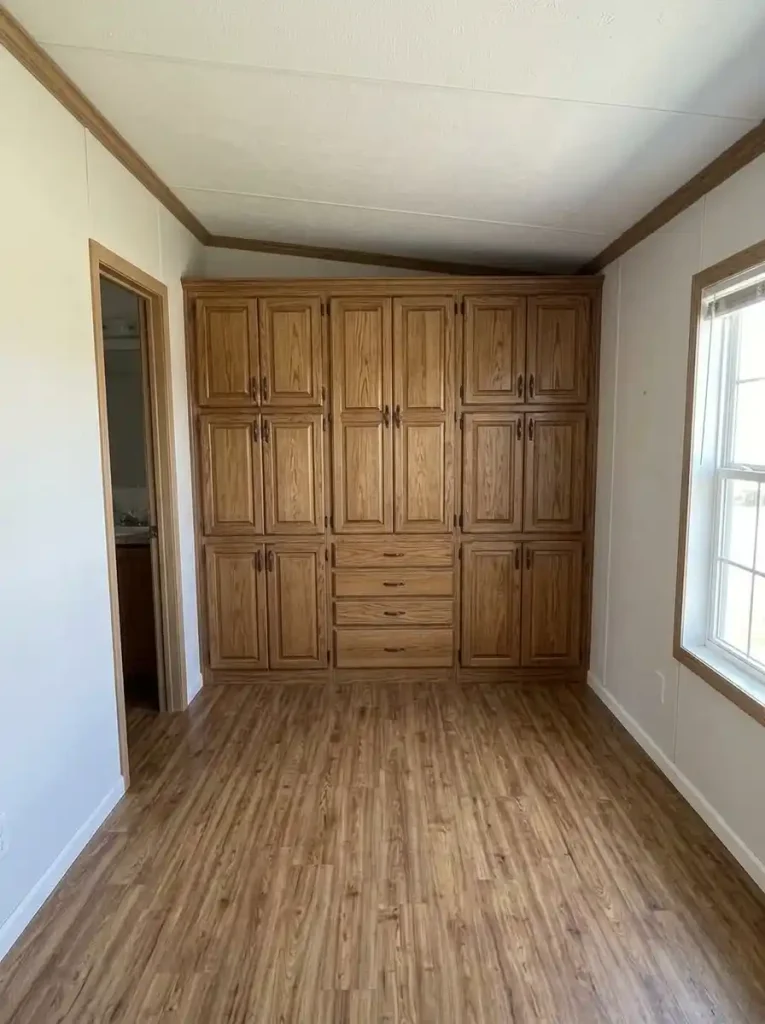 Deep storage cabinet placed on the short end wall of a single-wide room while the long passage walls stay comparatively shallow.