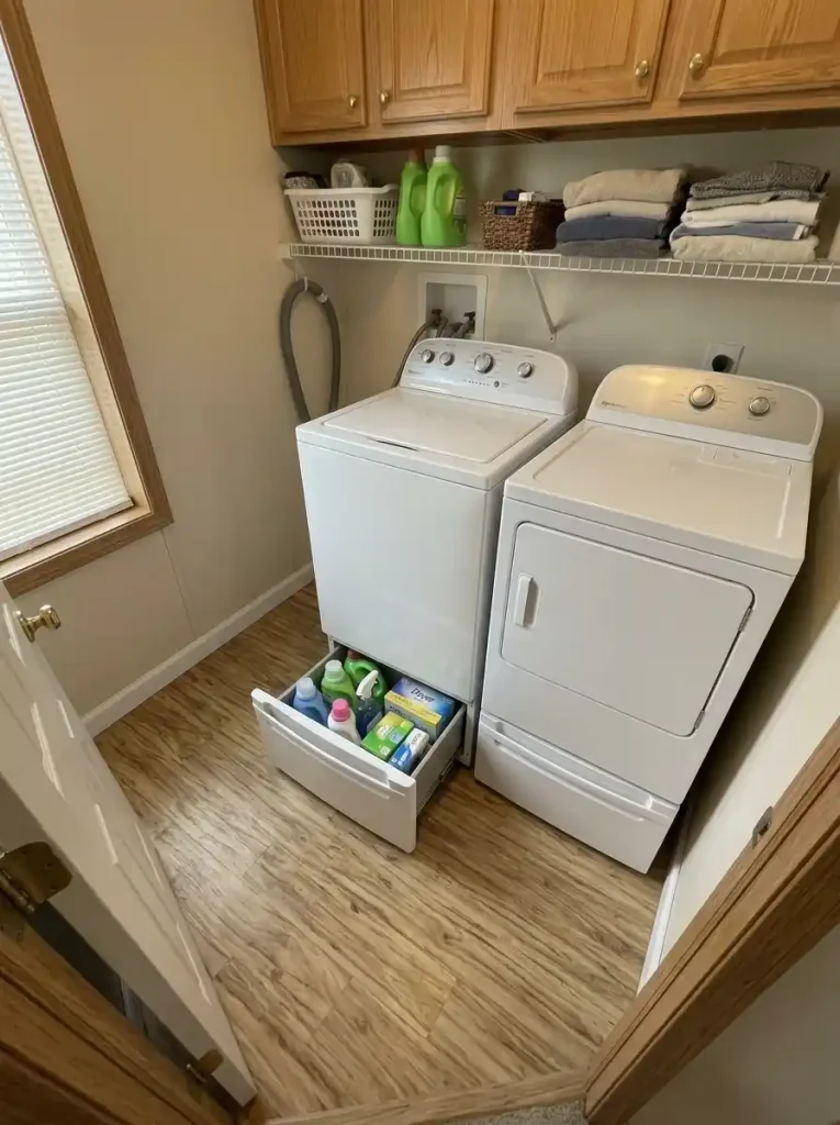 Washer and dryer on storage pedestals with laundry supplies inside the drawers and no separate floor cabinet beside them.