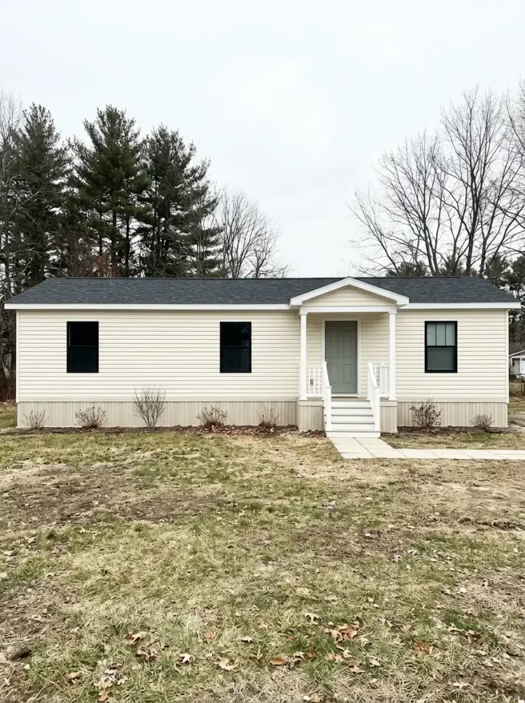 Cream single-wide manufactured home with a long shallow roofline, small front porch, and undecorated exterior.
