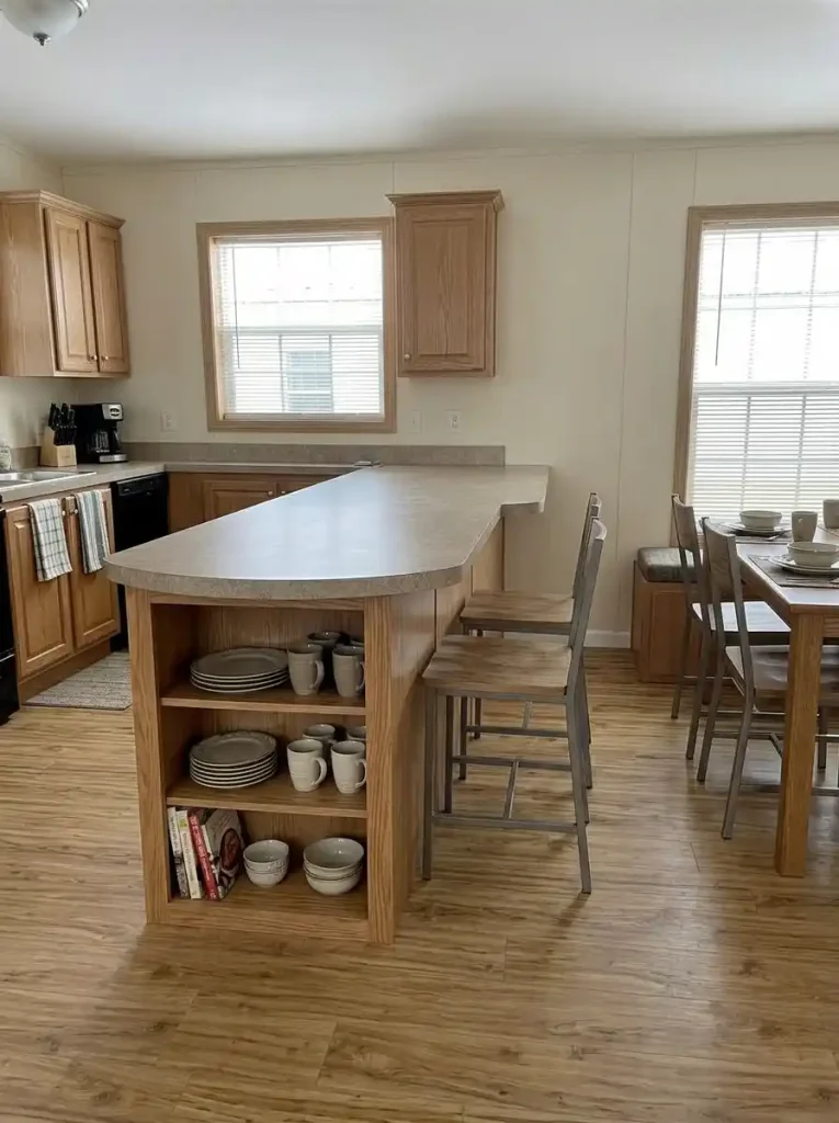 Shallow storage built into the living-room side of a single-wide kitchen peninsula while circulation around the end stays clear.