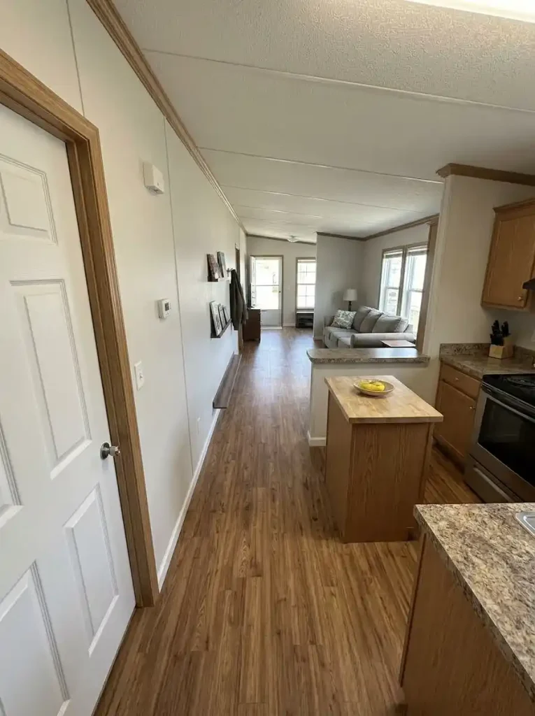 Long view through a single-wide home with storage positioned to preserve a straight walking route from the hallway to the entry.